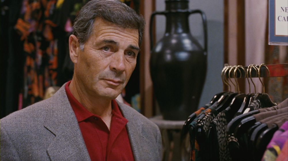 screenshot from Jackie Brown of Robert Forster's Max Cherry standing by dresses in the women's section of a department store. Forster is tan with blue eyes, a weathered face, slightly thinning salt & pepper hair. he's wearing a gray wool sport coat and a cherry-red polo shirt. 