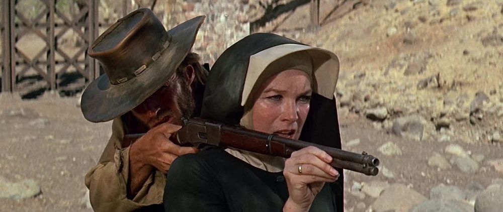 screenshot from Two Mules for Sister Sara feat. Clint Eastwood's very drunk Hogan propping his Winchester rifle on the right shoulder of Shirley MacLaine's Sister Sara. he's wearing a cowboy hat that obscures part of his face, she's wearing a nun's habit. 