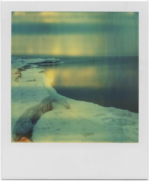 green-tinted polaroid of sky, a body of water to the right, and a frost or snow-covered beach/bank on the left with a slight crescent-shaped curve