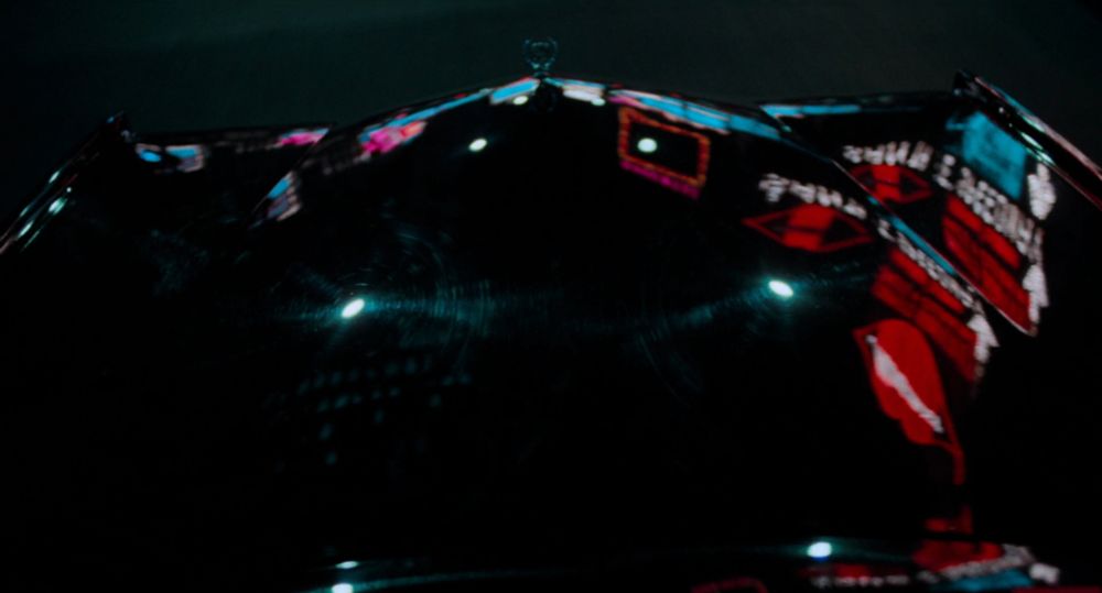 closeup on the black hood of a car at night with city lights reflected on its glossy surface 