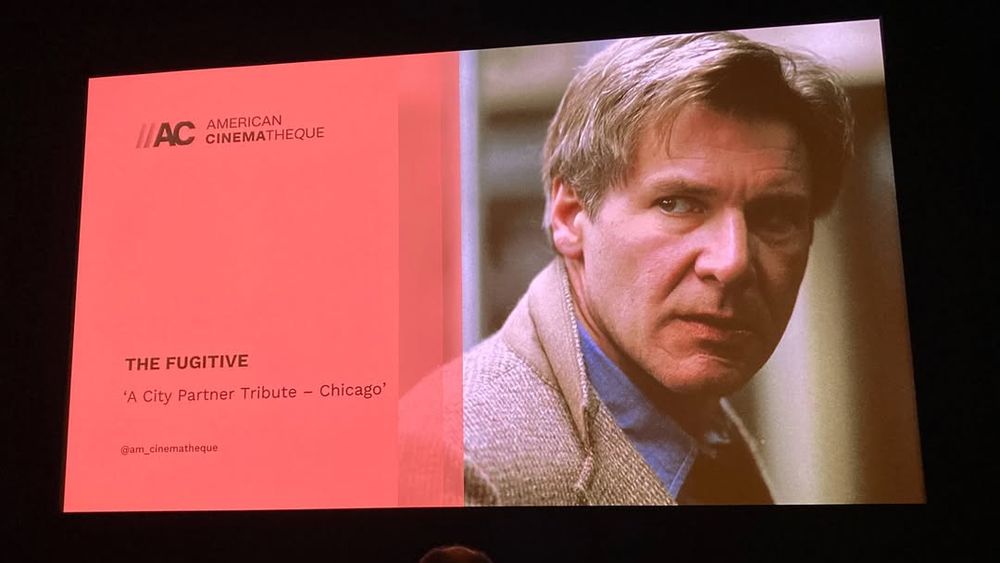 big movie screen with a salmony pink color on the left that reads "American Cinematheque - THE FUGITIVE - 'A City Partner Tribute - Chicago'" and a giant photo of handsome Harrison Ford on the right 