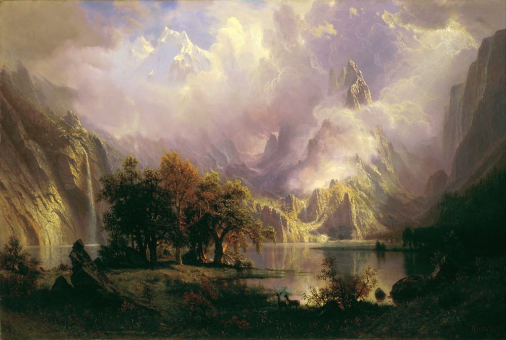 Albert Bierstadt’s Rocky Mountain Landscape, oil on canvas, 1870.
View of the Rocky Mountains, which dominate the painting - they're a mossy green, with one waterfall to the left and at least two narrow, silvery streams to the right. Some of the tallest peaks in the back are snow capped. in the foreground: a small copse of trees with green and orange leaves, a dark, shadowy meadow/grass with tiny pink flowers, a family of deer (doe, stag, fawn). The water between the mountains and the grass reflects the mountains almost perfectly. It's paradisiacal: the painting is about 40% clouds, which shift from pearlescent white to lavender (almost like moonstone) - they cling low to the mountains and climb up into the sky, obscuring its blue almost totally. Looks like the sun is in the upper right corner of the painting, though you can't see it, only its rays filtering through the clouds, touching the mountains and water below. 
