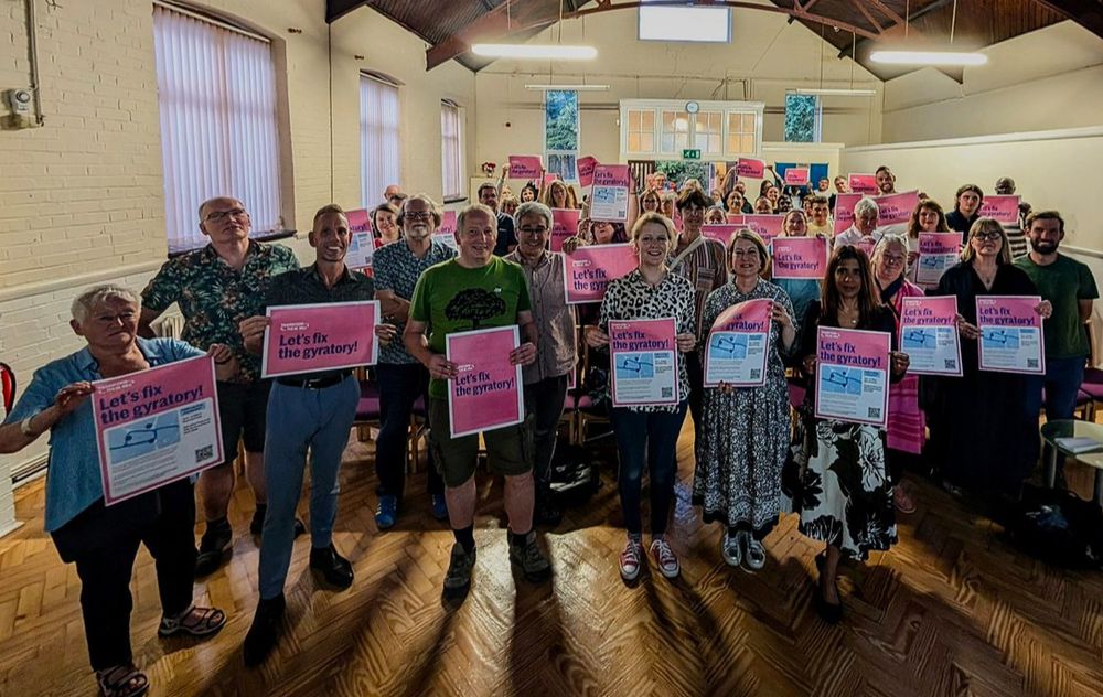 80 people at public meeting holding up signs saying 'Let's Fix The Gyratory"