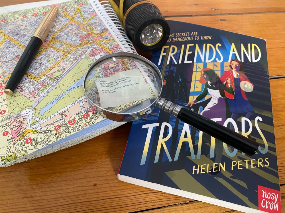 Copy of children’s mystery book Friends and Traitors, magnifying glass, pen, London A-Z, torch, coded message.