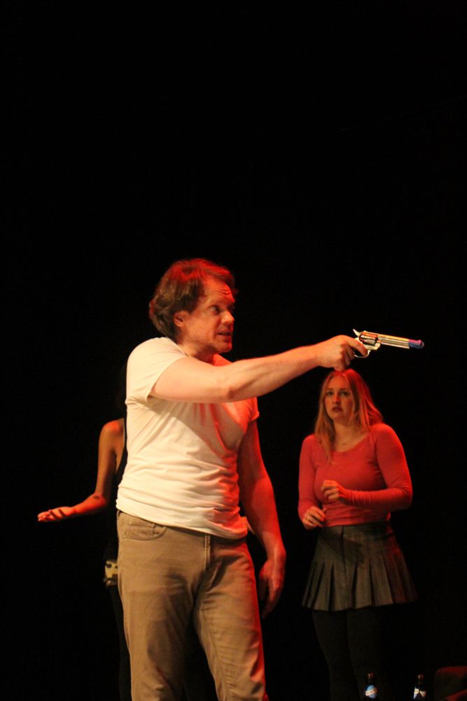 Me onstage pointing a prop gun threateningly to the right as two women cower in the background
