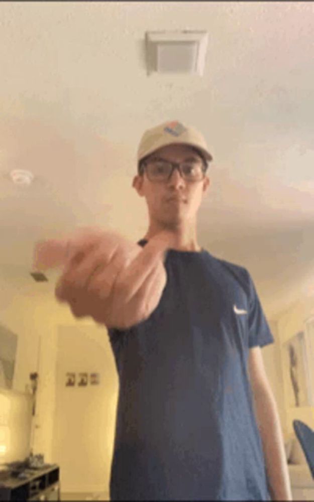 a man wearing glasses and a hat is giving the middle finger in a living room