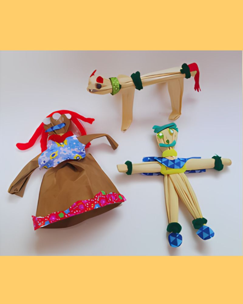 Three colorful, handmade dolls made from paper and cloth: a cat with a red tail, a woman in a floral dress, and a man in blue attire.