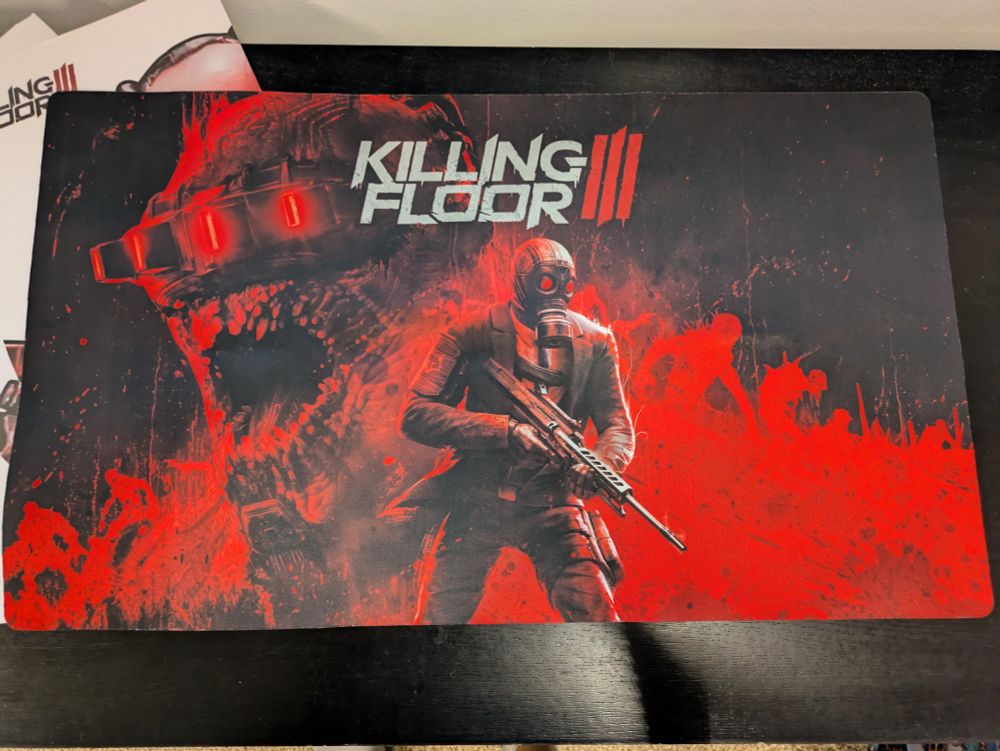 Large desk-sized mouse pad picturing a Killing Floor 3 survivor standing in front of a black-and-red oversized Zed bust