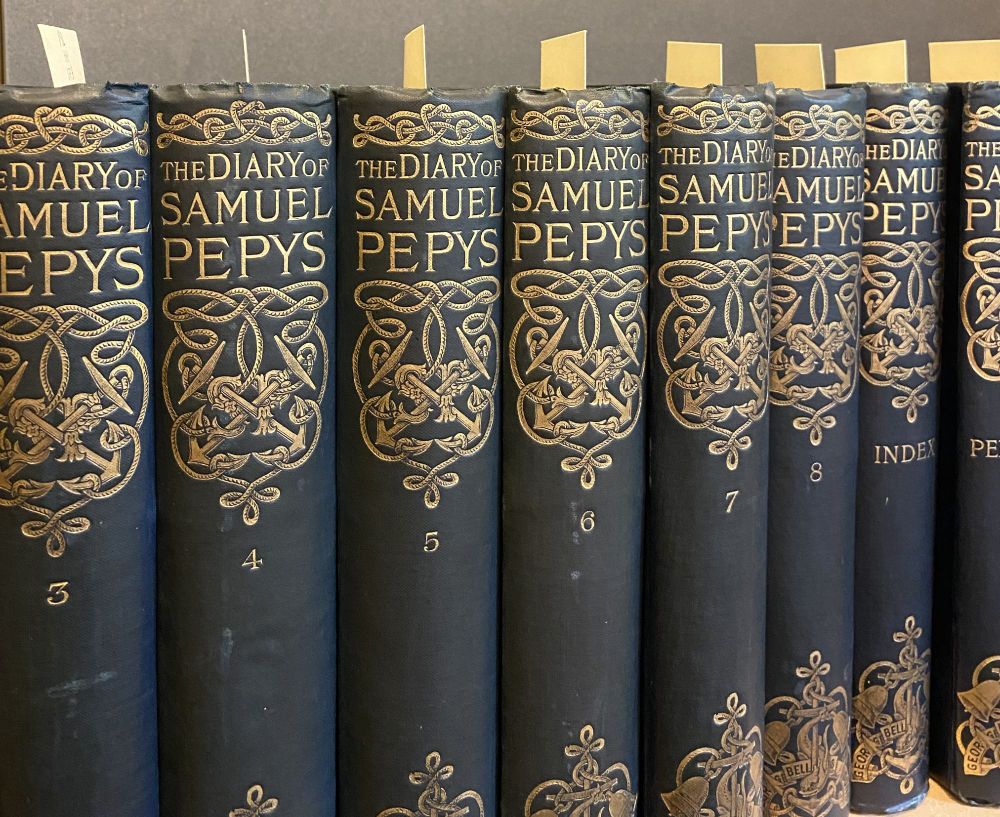Early printed editions of Samuel Pepys's diary on the shelves at Magdalene College, which are part of the Henk Hiltrop bequest.  The volumes have blue cloth covers with gilt lettering.