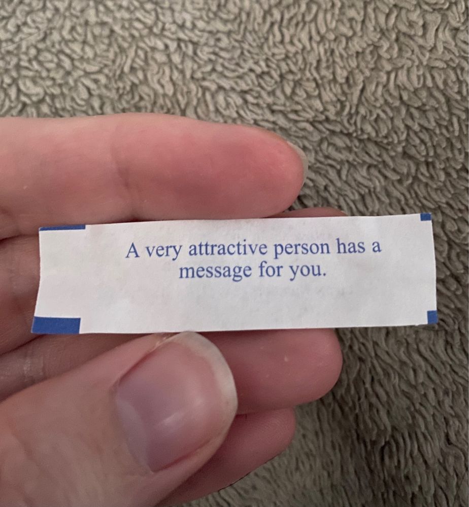 A hand is holding a fortune cookie message that says “A very attractive person has a message for you.”