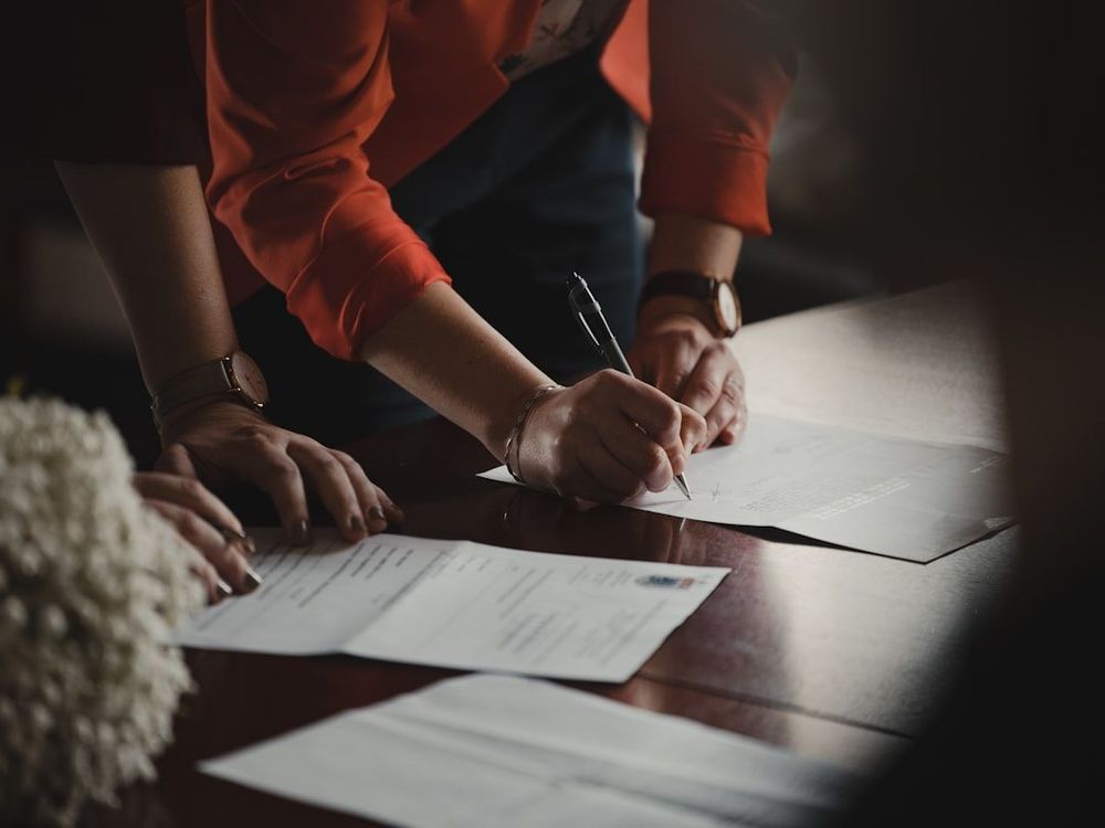 Photo of two people leaning over a desk signing documents. 