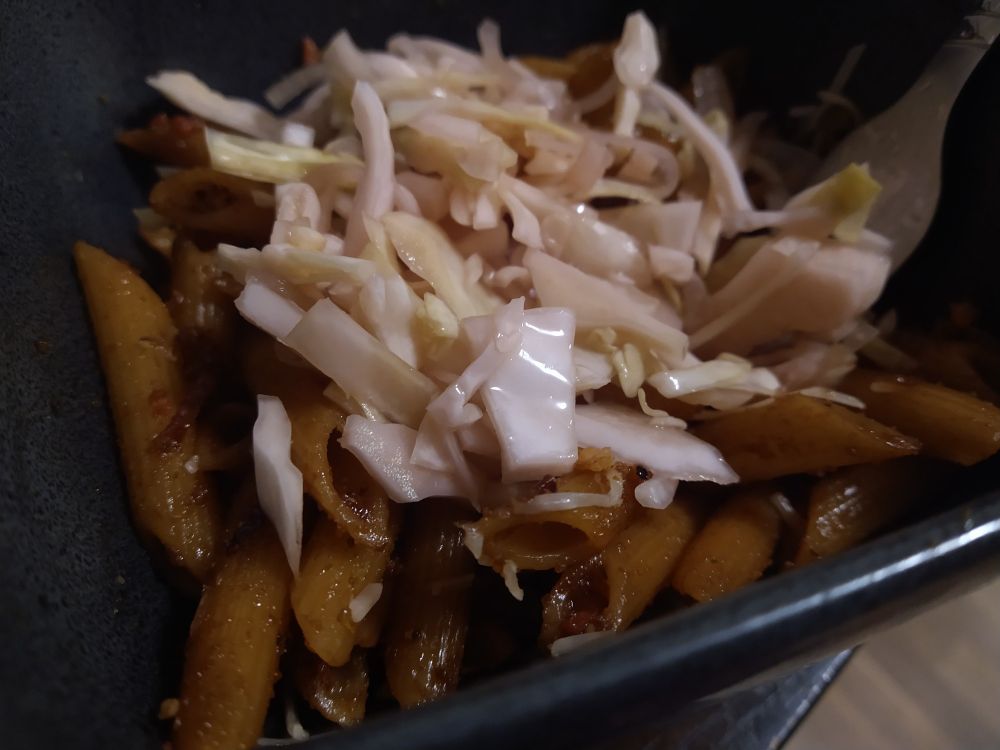 A bowl of fried penne noodles, dark with sauce, topped with chopped pickled cabbage