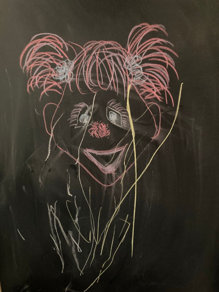 Chalk drawing of a pink muppet head with pink pom pig tails and several erratic yellow strokes over her face resembling flames