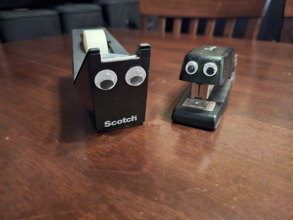 A tape dispenser and stapler with googly eyes.