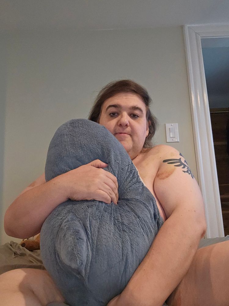 An image of a trans woman holding a blahaj.