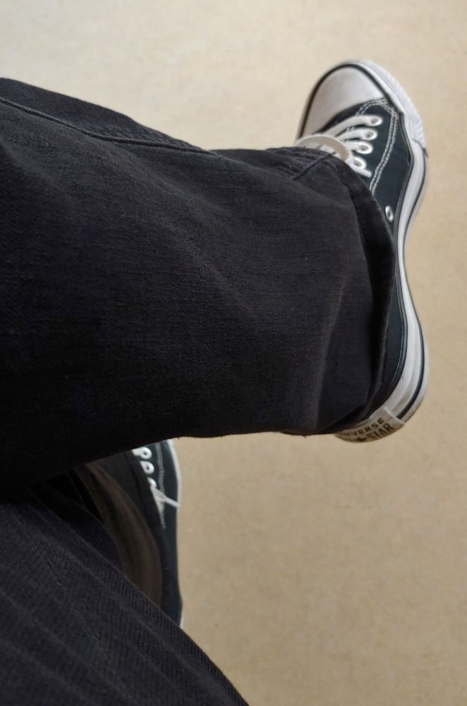 Ein überschlagenes Bein mit schwarzer Jeans und schwarzen Chucks 
