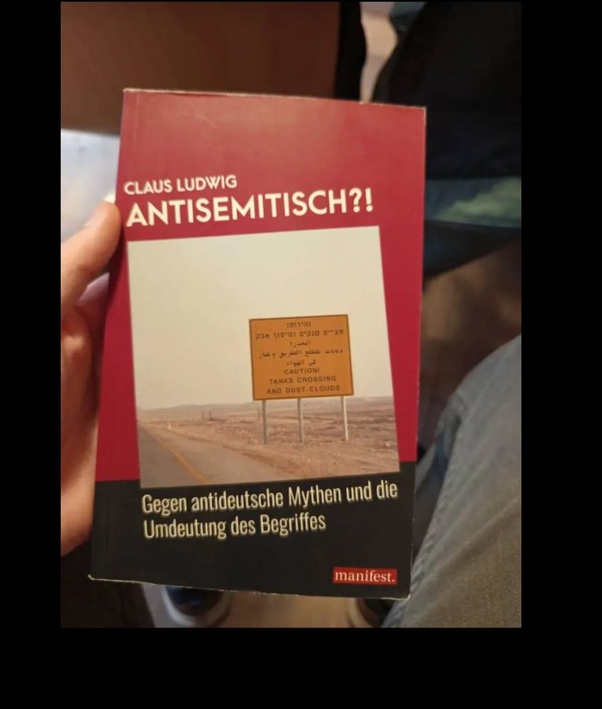 Buch mit schwarzroten Einband. Claus Ludwig, Antisemitisch?! Gegen antideutsche Mythen und die Umdeutung des Begriffes
Auf dem einband ist ein gelbes Schild mit in arabischer, hebräischer Schrift und auf Englisch steht dort Tanks crossing.