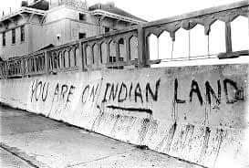 A black and white photo of a retaining wall at Alcatraz emblazoned with the words YOU ARE ON INDIAN LAND 