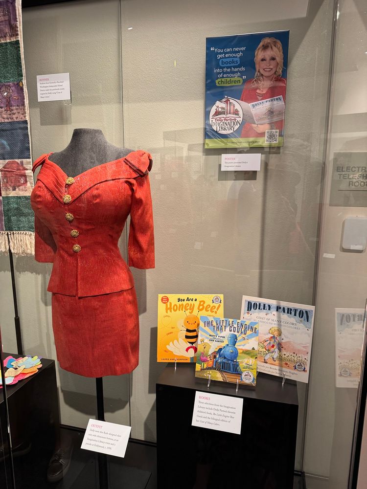 Red dress in glass display case along with three picture books 