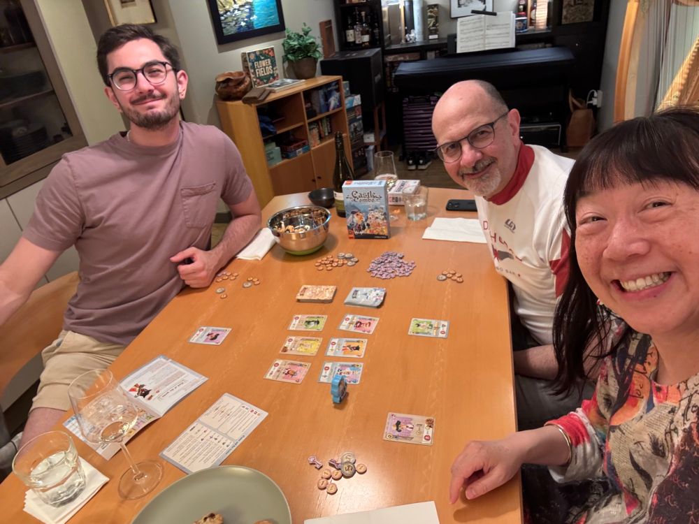 Three people sitting around a table, playing a card game. 
