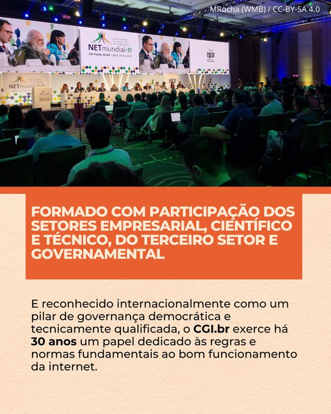 Fotografia de um auditório durante um evento. Ao fundo, um palco iluminado com um grande telão exibindo o logo "NETmundial+10 São Paulo, Brasil April 29-30, 2024" e "cgi.br", além de imagens de palestrantes. No palco, diversas pessoas estão sentadas em uma longa mesa. Em primeiro plano, o público está sentado em cadeiras verdes, de costas para a câmera, assistindo ao evento. Sobreposta à imagem, na parte inferior, uma faixa laranja com o texto em letras brancas maiúsculas: "FORMADO COM PARTICIPAÇÃO DOS SETORES EMPRESARIAL, CIENTÍFICO E TÉCNICO, DO TERCEIRO SETOR E GOVERNAMENTAL". Abaixo desta faixa, em um fundo branco, o texto em preto: "E reconhecido internacionalmente como um pilar de governança democrática e tecnicamente qualificada, o CGI.br exerce há 30 anos um papel dedicado às regras e normas fundamentais ao bom funcionamento da internet.". No canto superior direito da imagem, a legenda "MRocha (WMB) / CC-BY-SA 4.0".