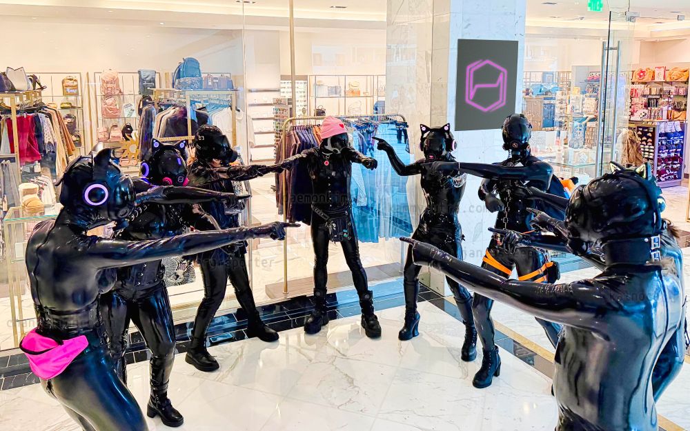 8 latex drones in a circle all pointing at each other, like the spiderman meme. The store sign has been changed to the Hexcorp logo.