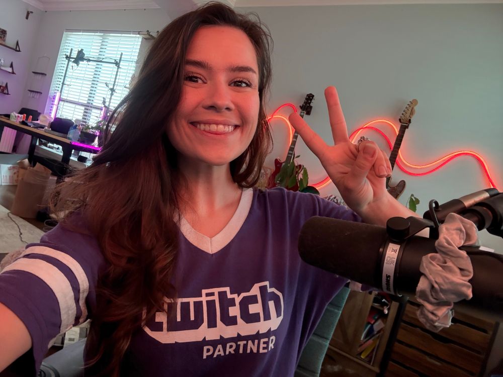 Selfie of me at my desk with long brown hair and I’m wearing my purple twitch shirt