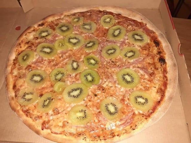 A pizza topped with strips of some kind of meat, cheese, and kiwis