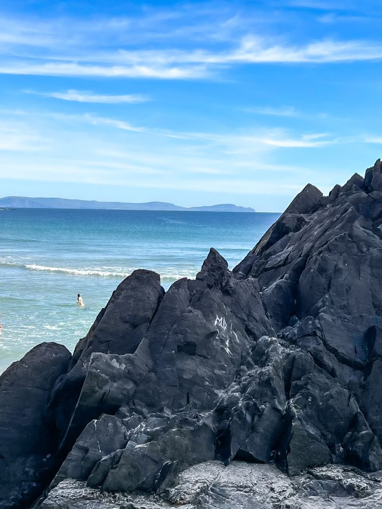 A bather in the distance beyond the jagged volcanic stones enjoys the gentle waves of  the Big Island of Hawaii
