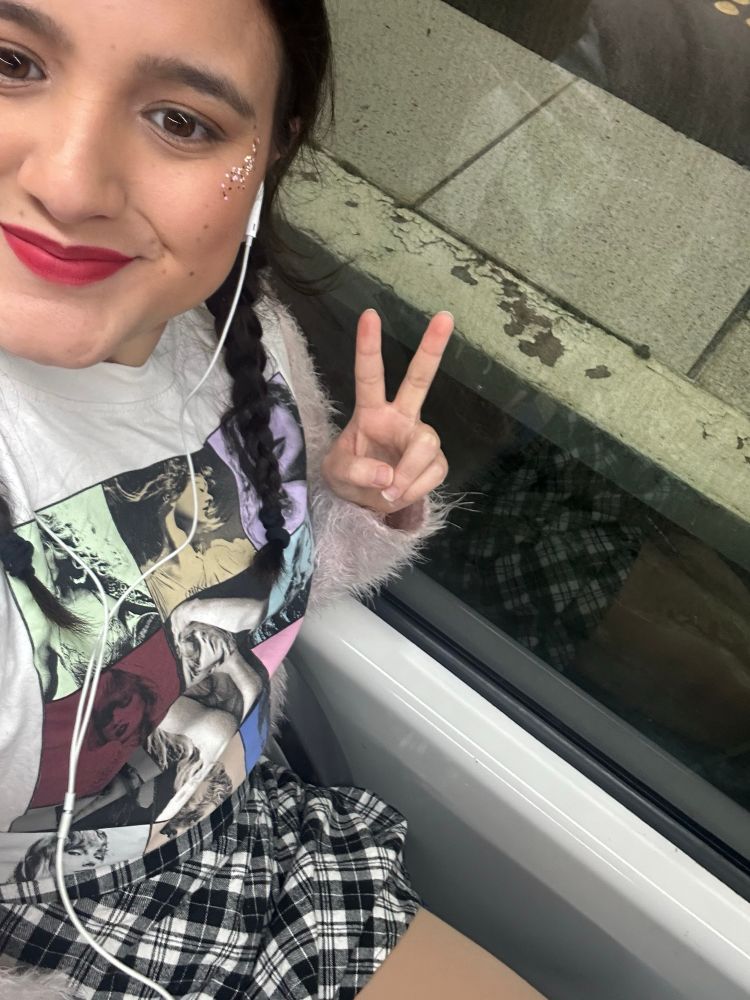 person sitting with a taylor swift shirt, black and white plaid skirt, red lipstick and glitter