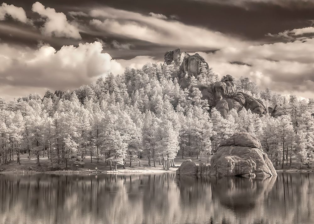 Infrared, monochrome image glowing trees, rock outcroppings, soft reflections, and cloud-filled skies at Sylvan Lake in Custer State Park in South Dakota. 