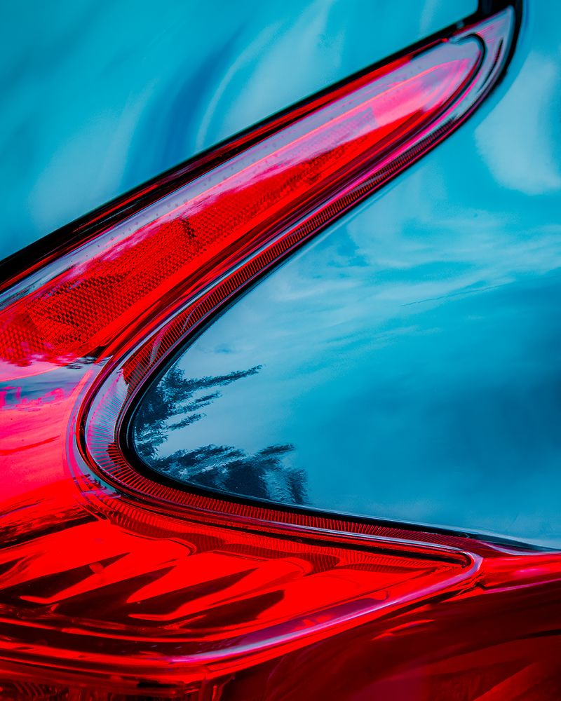 Close-up of a bright red taillight with the sky reflected in the metal of a light blue car.