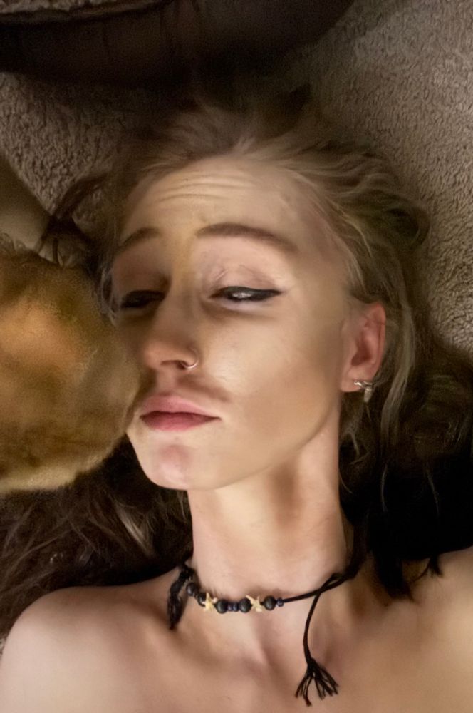 K in light drag king makeup letting their blur of an orange cat inspect their fake mustache
