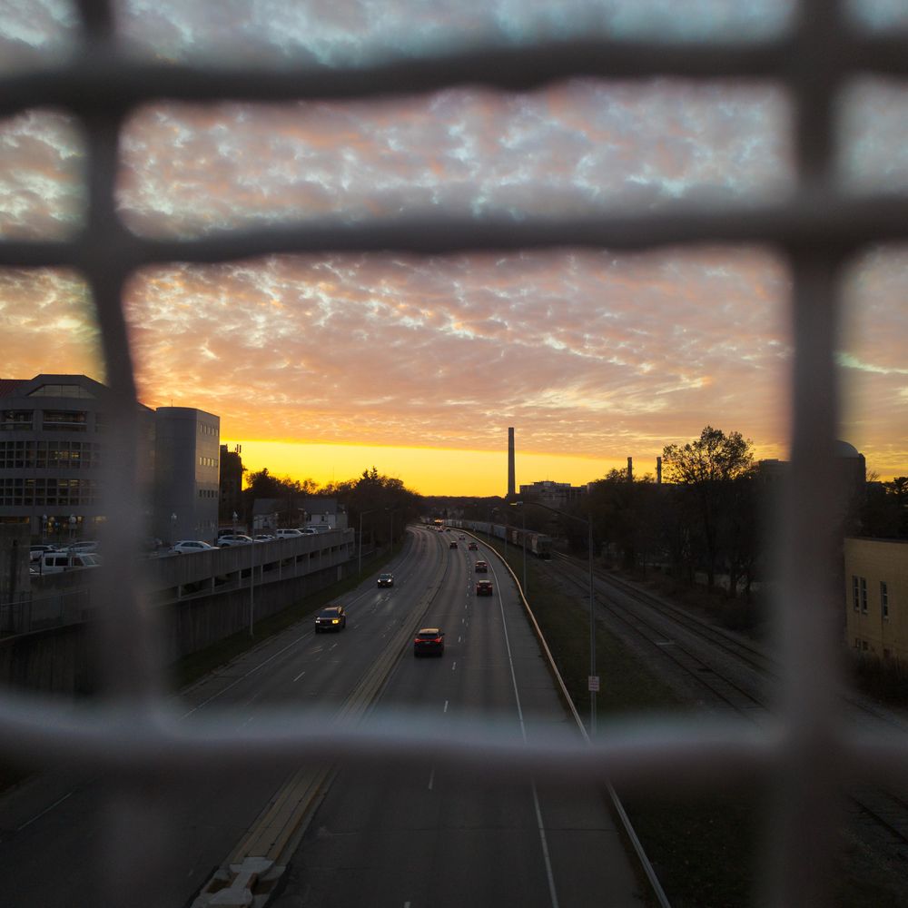 A square photo taken from the Alicia Ashman overpass looking west over Campus Drive. The sun is below the horizon already and a sharp line separates a sliver of clear sky from a layer of clouds.