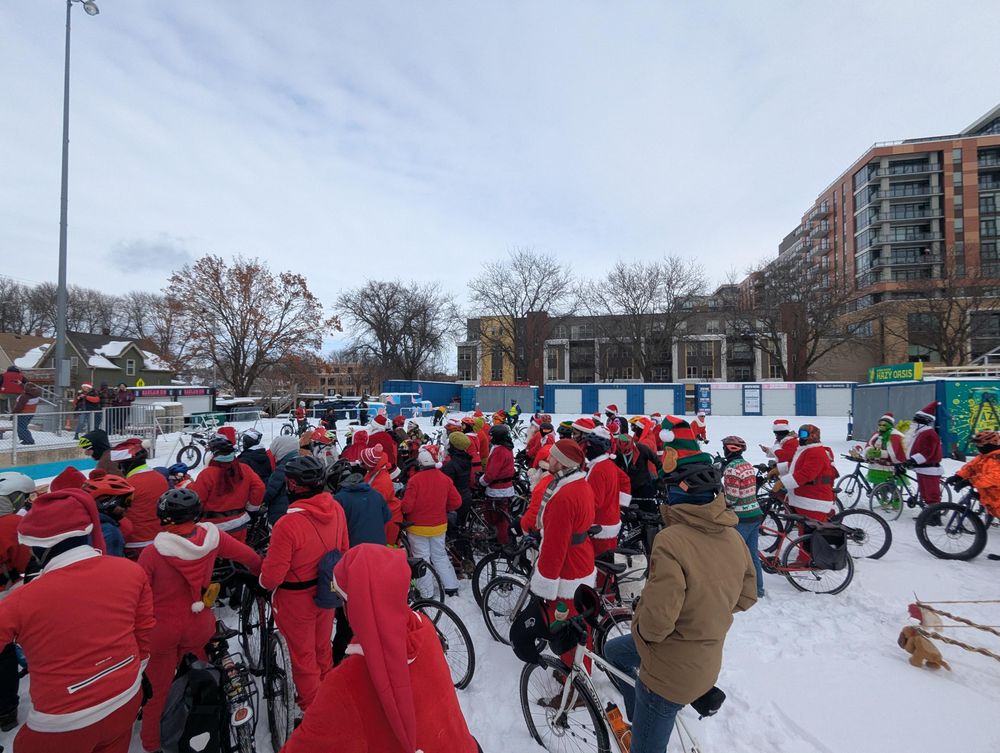 A crowd of people in Santa outfits and with bikes on Breese Stevens Field, which is solidly covered in snow.