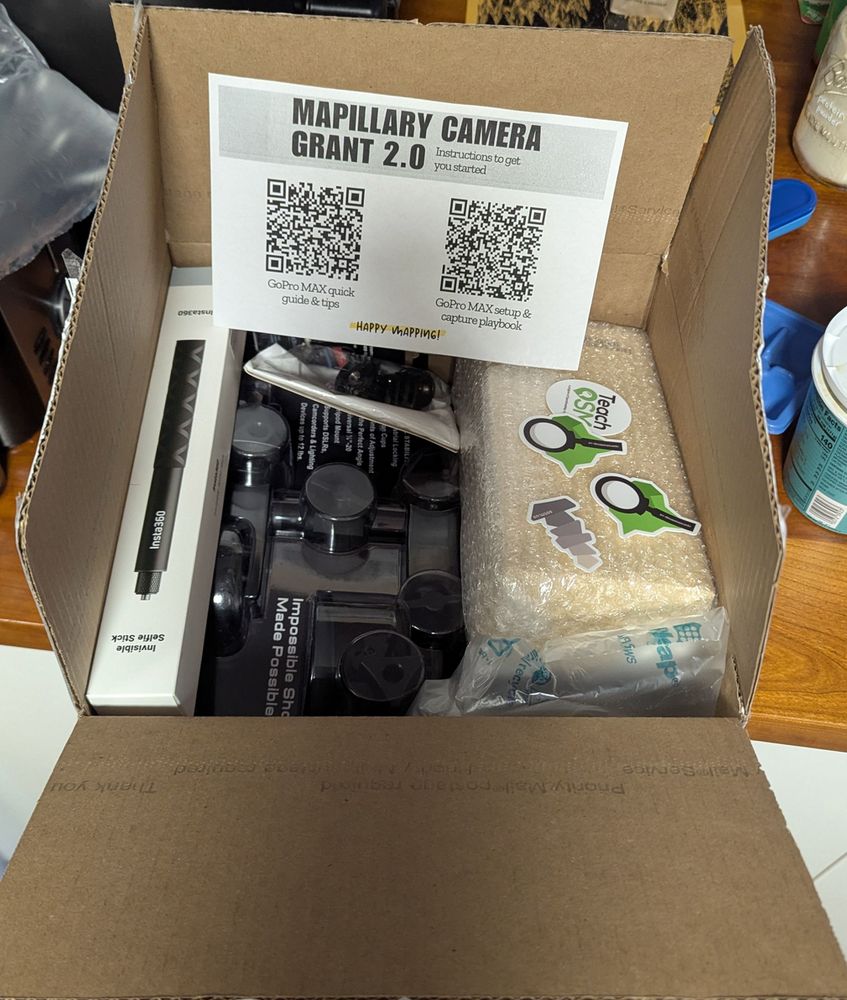 An opened cardboard box with a variety of action cam supplies and a few OpenStreetMap stickers.