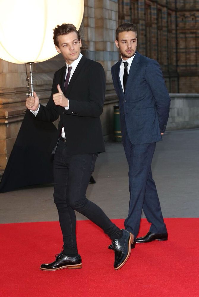 Louis Tomlinson and Liam Payne dressed in suits and walking on a red carpet 