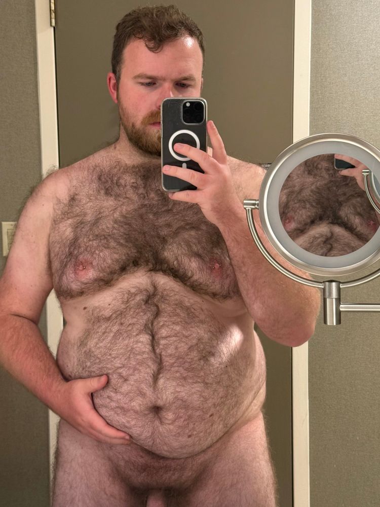 Mirror selfie. I’m nude, holding my belly up. Cropped from the base of my dick up. There’s a small, wall mounted mirror focusing on my chest in front of me. 