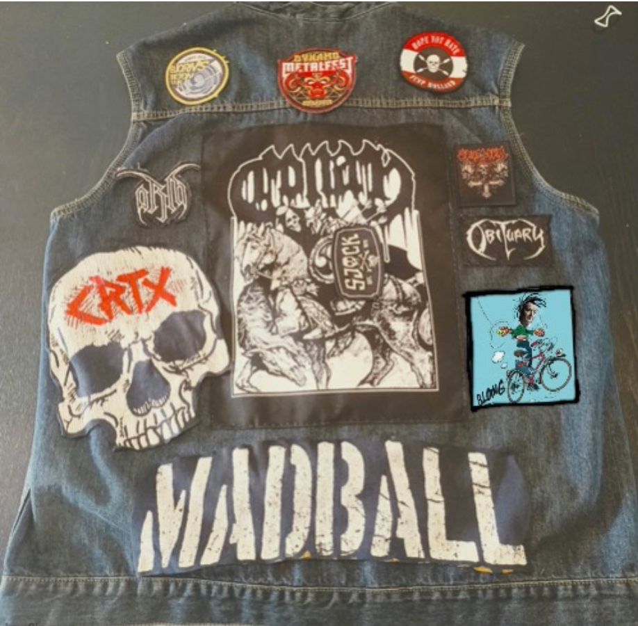 Een kek-spijkerjekkie zonder mouwen met op de rug patches o.a. Dynamometalfest, orbituary, Madball en een punkhans op touwtje springende fiets