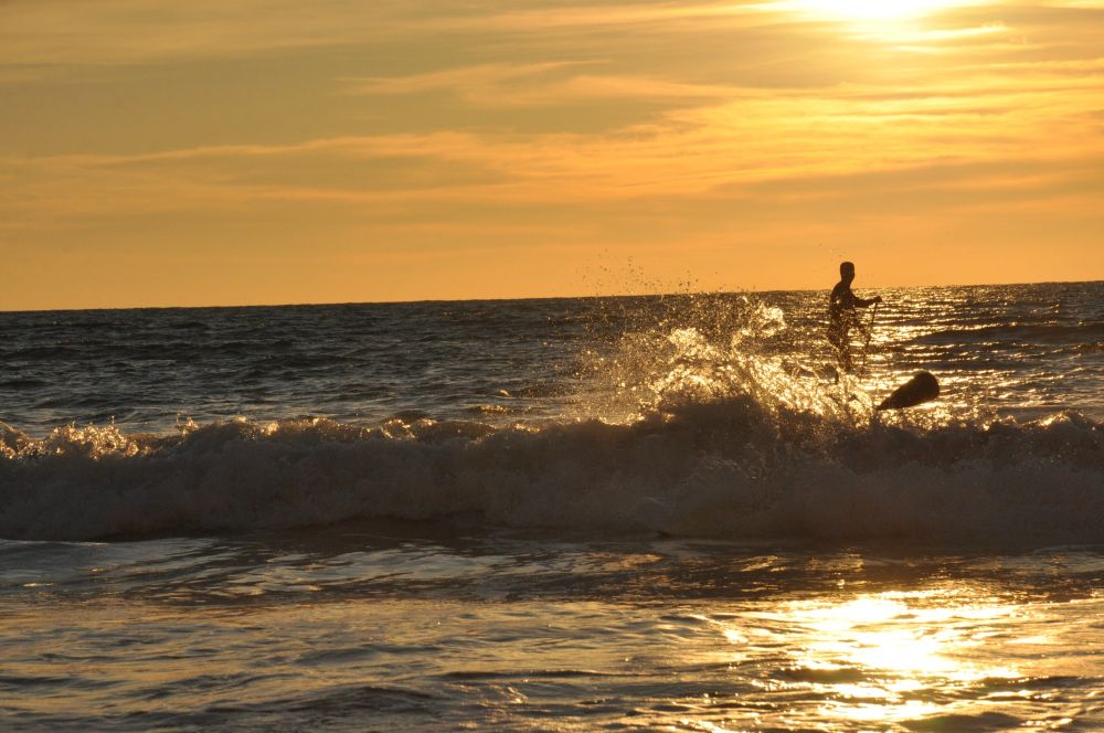 foto de un atardecer, con el mar oscuro y el cielo amarillo. Un hombre hace surf