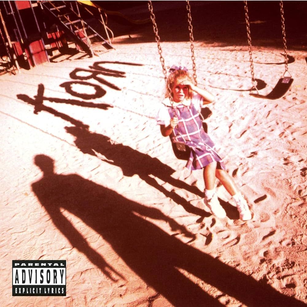 Couverture de l'album éponyme de Korn.
Une petite fille sur une balançoire à l'arrêt regarde vers l'objectif en protégeant ses yeux du soleil avec sa main, on voit l'ombre gigantesque et inquiétante d'un homme qui lui fait face hors-cadre.
C'est un album fondateur du genre "Nu-metal" ou "Neo-metal".
