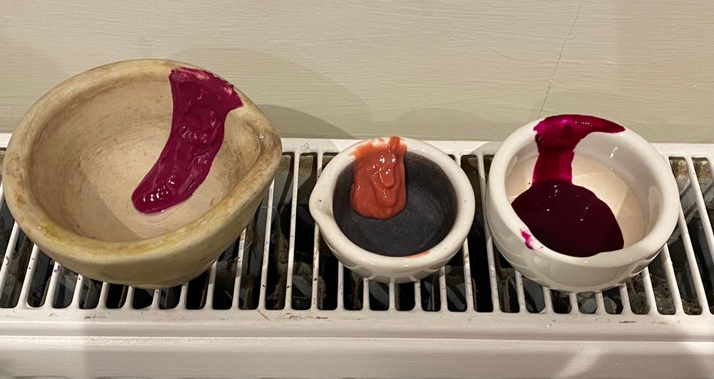 Deep pink, peach-coloured and dark magenta precipitates drying in small mortars over a radiator 