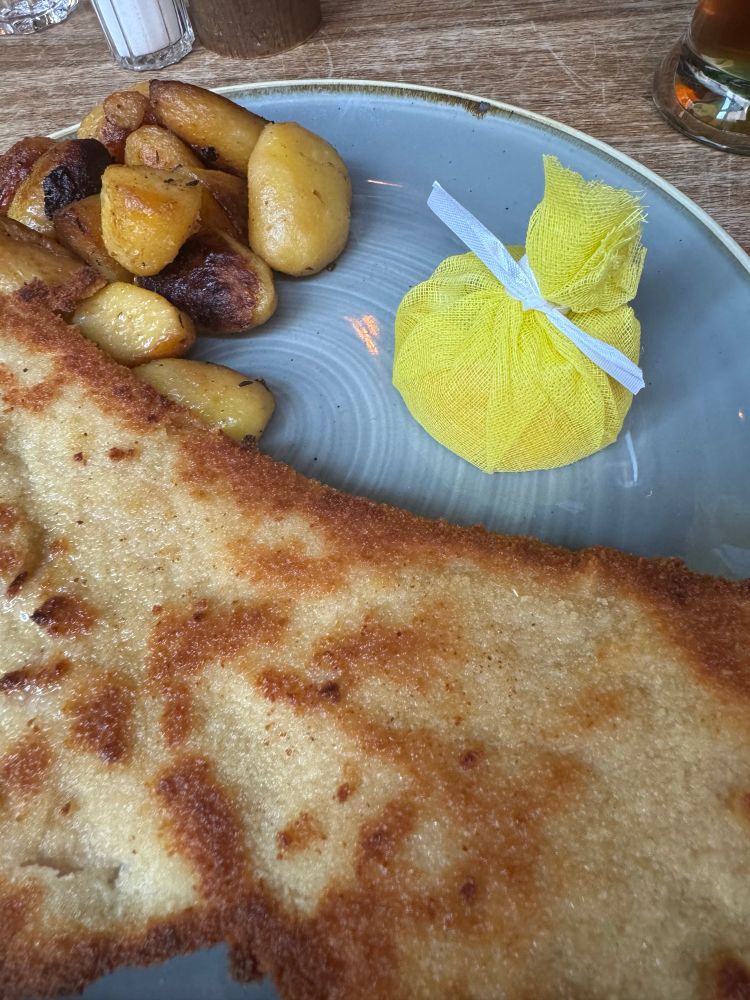 Ein Teller mit einem Schnitzel. Die Zitrone ist in einem gelben Säckchen verpackt
