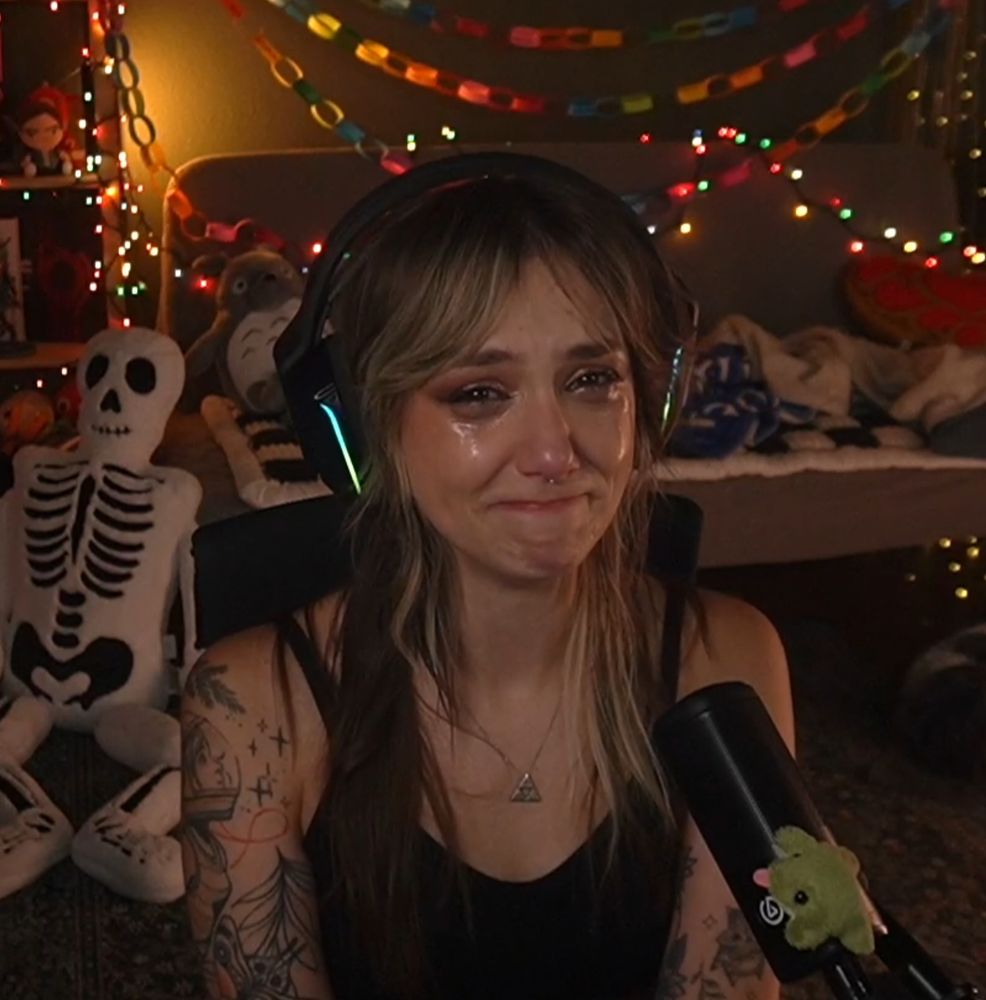 a screencap from ellie's stream where she is visibly crying but looking at the camera with a sad smile