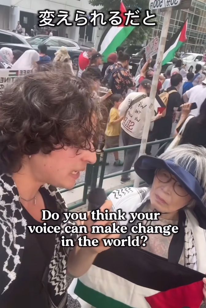 a person interviewing an older japanese woman wearing a sun hat and keffiyeh and holding a handmade palestinian flag bag at a march for Gaza in Tokyo. the interviewer asks in Japanese: “do you think your voice can make change in the world?”

東京のガザのためのマーチで、人はおばあさんとインタビュウしています。人はおばあさんと質問している「自分の声で何か変えられるだとと思いますか？」