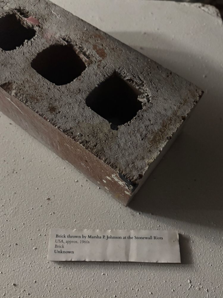 a brick on top of a white museum pedestal with a placard reading:

Brick thrown by Marsha P. Johnson at the Stonewall Riots
USA, approx. 1960s
Brick
Unknown 
