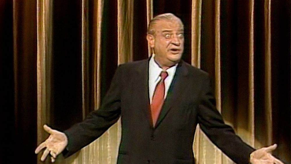 Rodney Dangerfield, arms outstretched, having just delivered a punchline