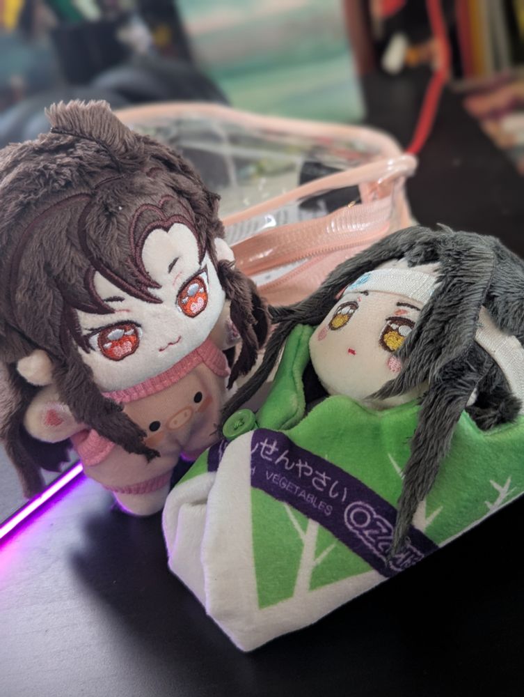 Cotton dolls Wei Wuxian and Lan Wangji. Wei Wuxian is dressed in a pink pig jumper, while Lan Wangji is swaddled in a cabbage leaf.