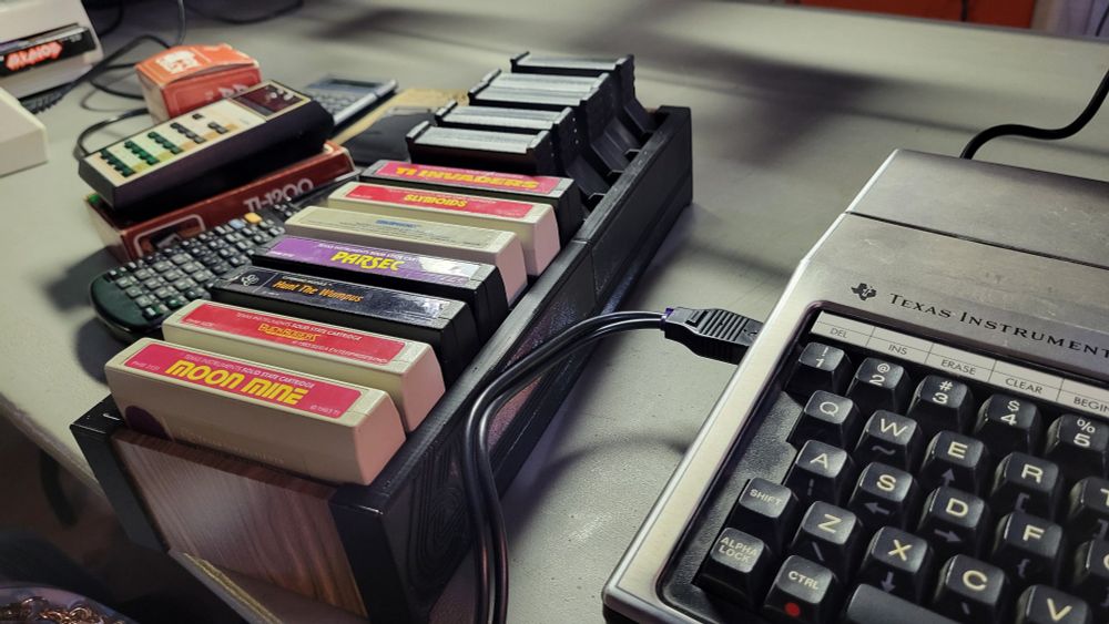 A series of TI-99 cartridges on a desk next to the vintage computer and some calculators.