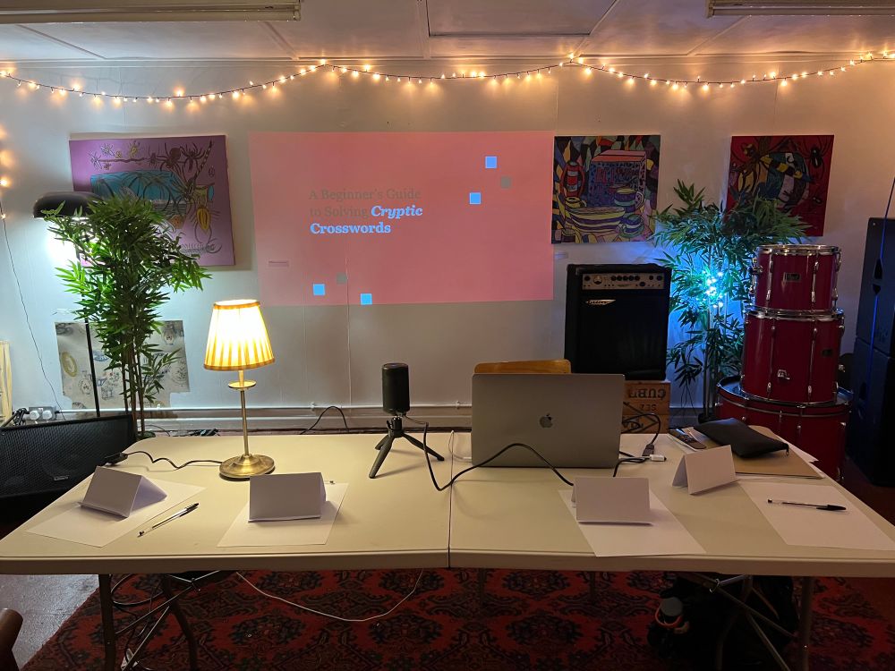 A table with paper and pens. Projection of a slide “Cryptic Crosswords for Beginners” 